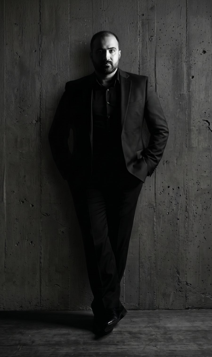 Ali Abdullateef, full-length portrait against a board-formed concrete wall